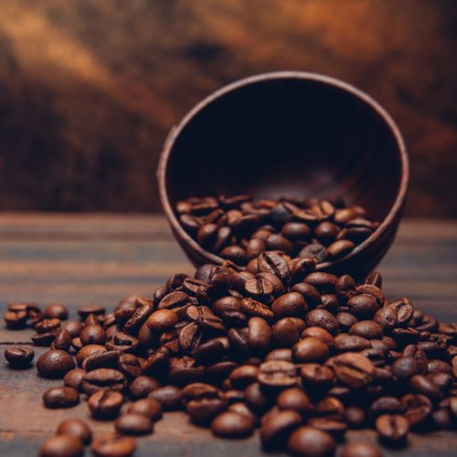 Dark coffee beans in a bowl on a brown background. side view.